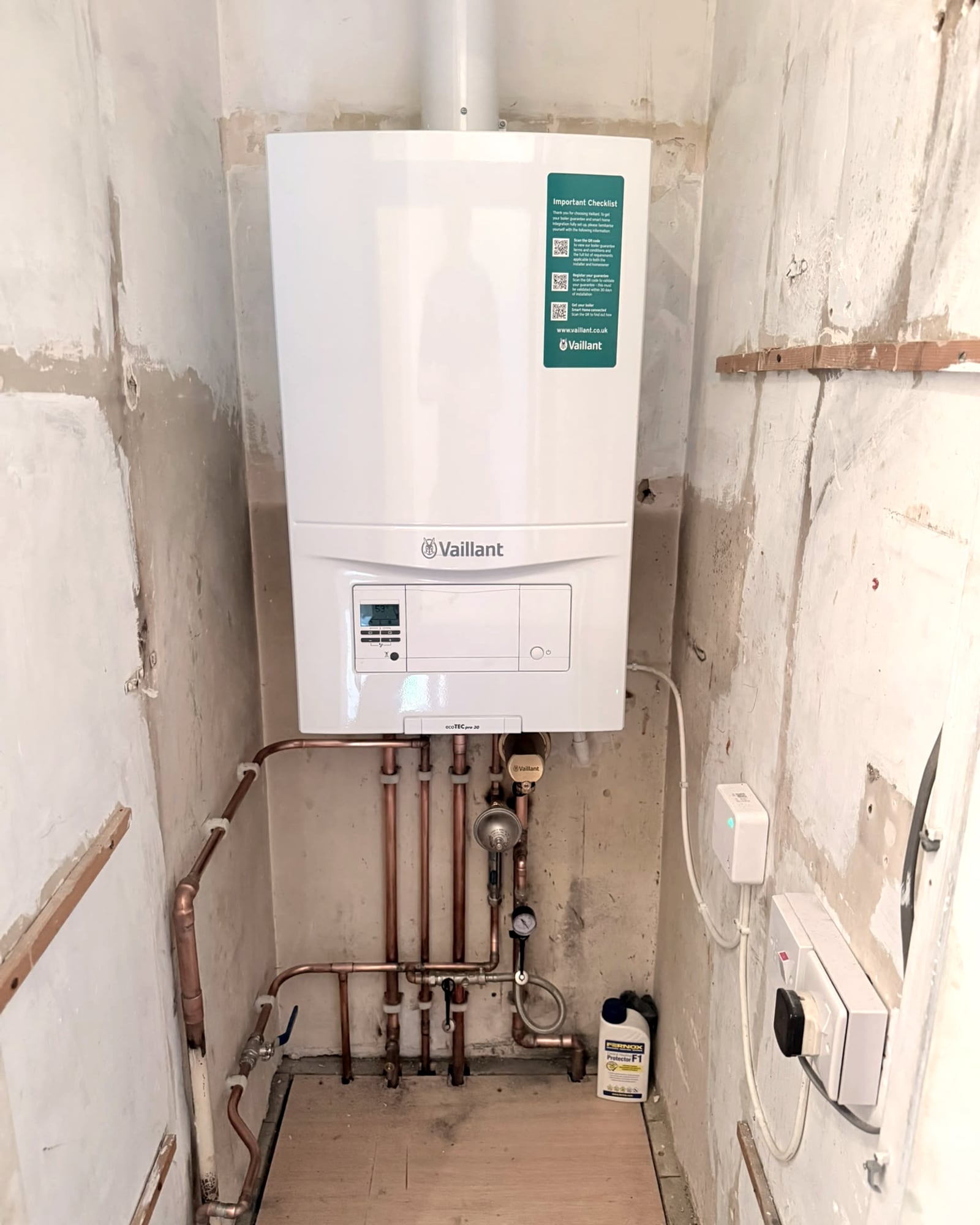 A Vaillant combi boiler in a narrow cupboard with straight copper pipework and a filter below